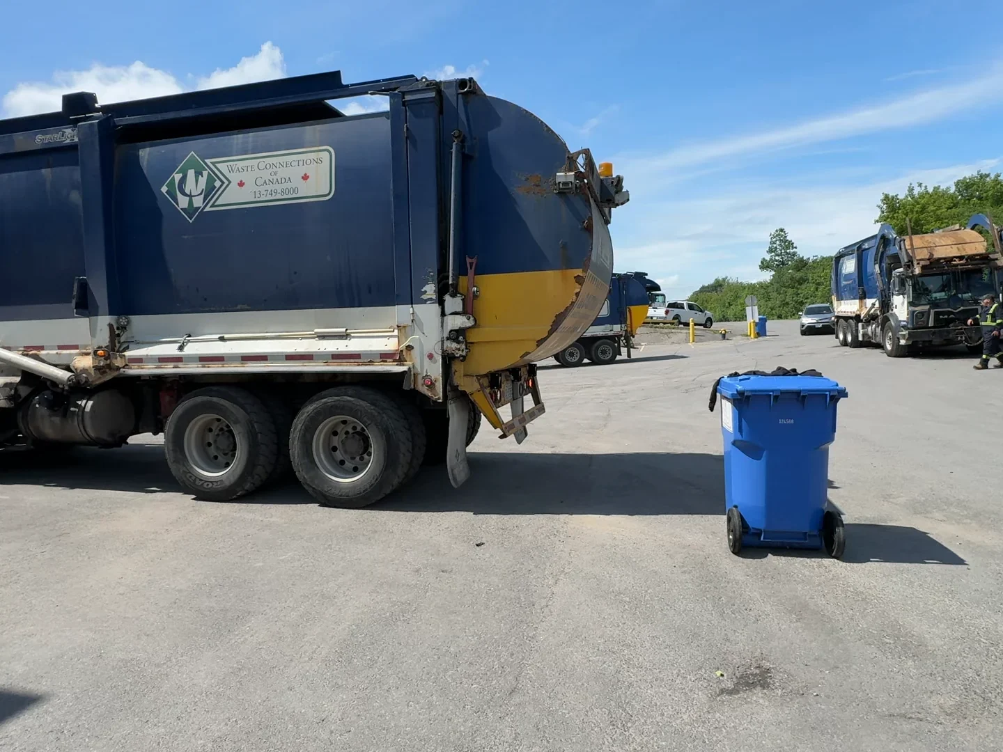 Waste Connections front-load truck in a yard beside a blue recycling cart