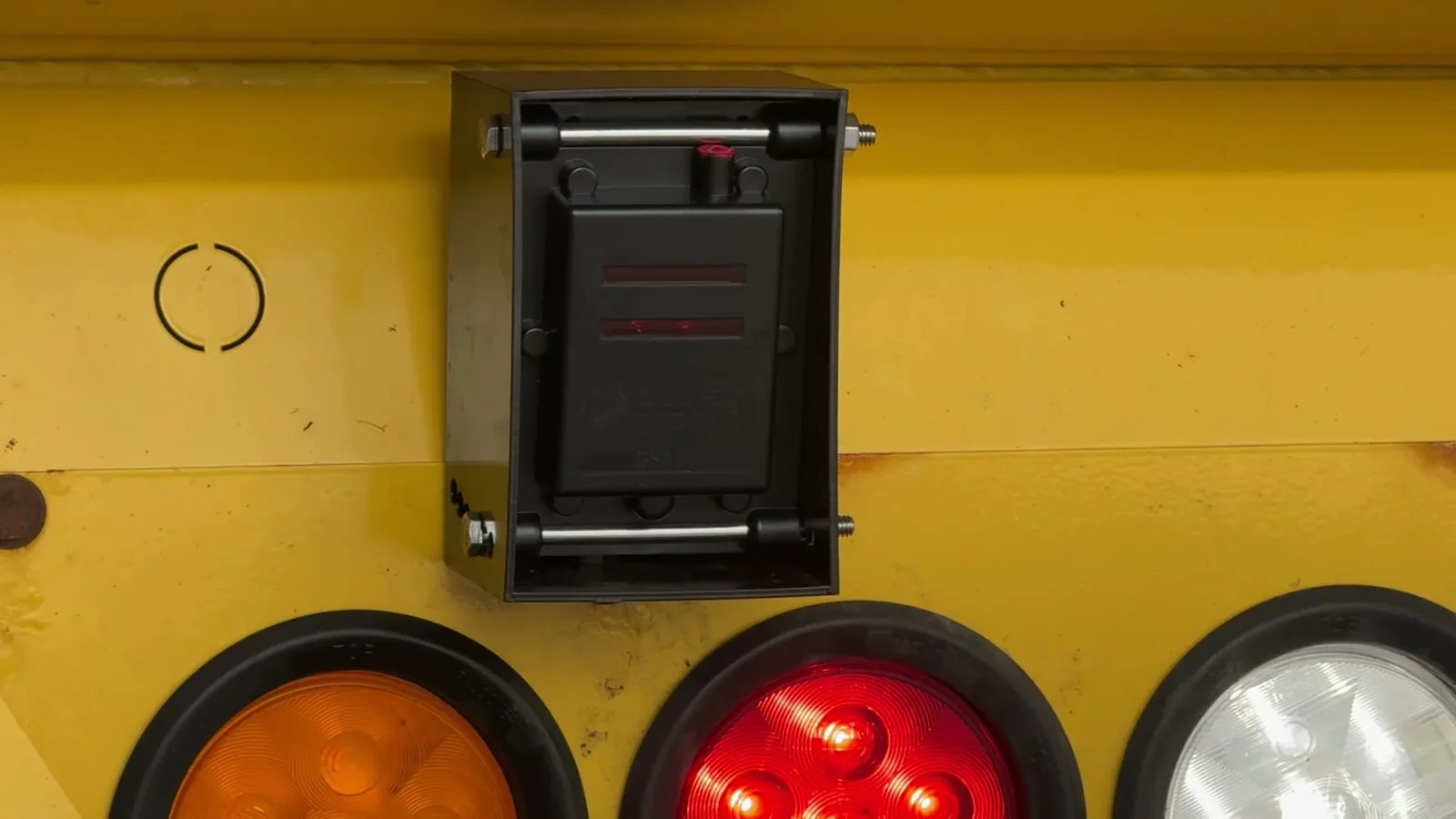 Sensor mounting box on the rear of a yellow truck, above the tail lights